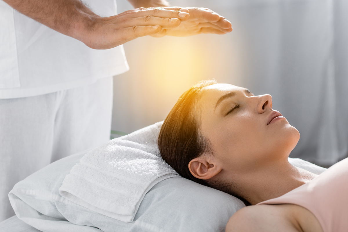 Hands with a glowing powerful light over a woman’s forehead to show Reiki healing.